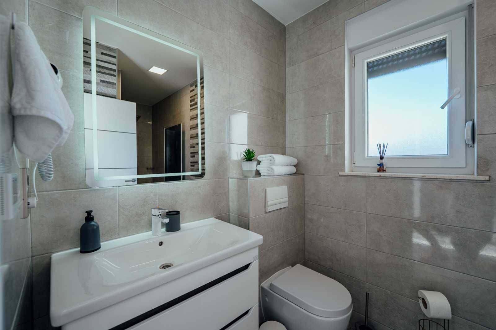 Une salle de bain moderne avec un lavabo blanc, des toilettes, un miroir et une fenêtre.