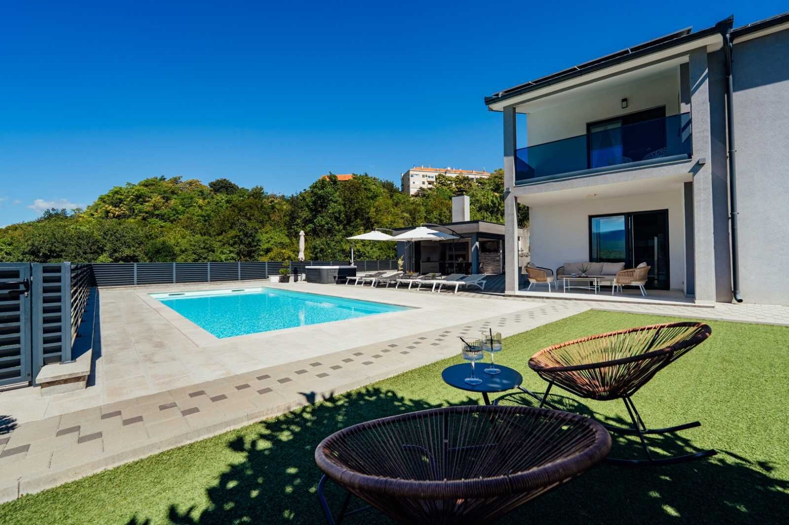 A modern house with a swimming pool, outdoor seating, and a view of the surrounding area.