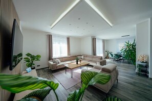 Ein modernes Wohnzimmer mit einem Ecksofa, einem Couchtisch und einem an der Wand montierten Fernseher.