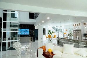 A modern interior with a glass partition, a white sofa, a dining area, and a kitchen.