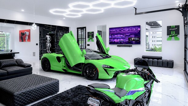 Una sala de estar moderna con un coche deportivo verde, una motocicleta, un sofá y un televisor mostrando un juego de carreras.