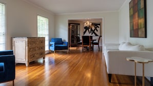 Ein geräumiges Wohnzimmer mit Holzdielen, einem weißen Sofa, einem blauen Sessel und einem Holzschrank.