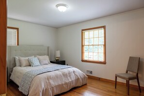 Ein Schlafzimmer mit Bett, Nachttisch, Lampe, Stuhl, Fenster und Deckenleuchte.