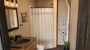 Un baño con tocador de madera, inodoro, ducha con cortina y una pequeña planta en maceta.