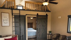 Un dormitorio con cama, escritorio, silla, ventilador de techo y una escalera.