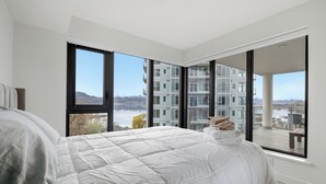 A bedroom with a large bed, a view of buildings, and a balcony. - Premiere Lakeshore Living with excellent amenities. Dog friendly (Kelowna)