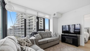 A modern living room with a sofa, TV, and large windows overlooking a building. - Premiere Lakeshore Living with excellent amenities. Dog friendly (Kelowna)