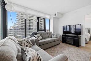 A modern living room with a sofa, TV, and large windows overlooking a building.