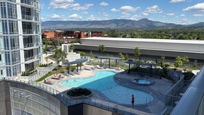 A rooftop pool with a view of mountains, a modern building with glass windows, and a landscaped area with lounge chairs. - Premiere Lakeshore Living with excellent amenities. Dog friendly (Kelowna)