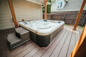 Ein Whirlpool auf einer Holzterrasse mit einer Holzbank und einer Pergola darüber.