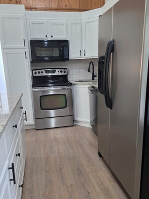 Eine Küche mit weißen Schränken, einem Edelstahlbackofen, einer Mikrowelle, einem Kühlschrank und einem Holzboden.
