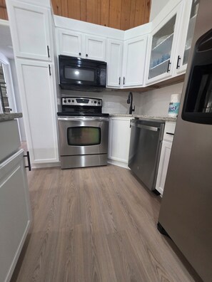 A kitchen with white cabinets, stainless steel appliances, and a wooden floor. - Lake Lanier Getaway. Hot Tub & Fire Pit. 5-Min Walk to Lake Access (Flowery Branch)