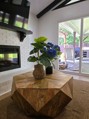 A modern interior with a wooden coffee table, a fireplace, and a view of the outdoors. - Lake Lanier Getaway. Hot Tub & Fire Pit. 5-Min Walk to Lake Access (Flowery Branch)