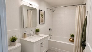 Ein Badezimmer mit Toilette, Waschbecken, Spiegel, Dusche und einem kleinen Regal mit einer Pflanze.
