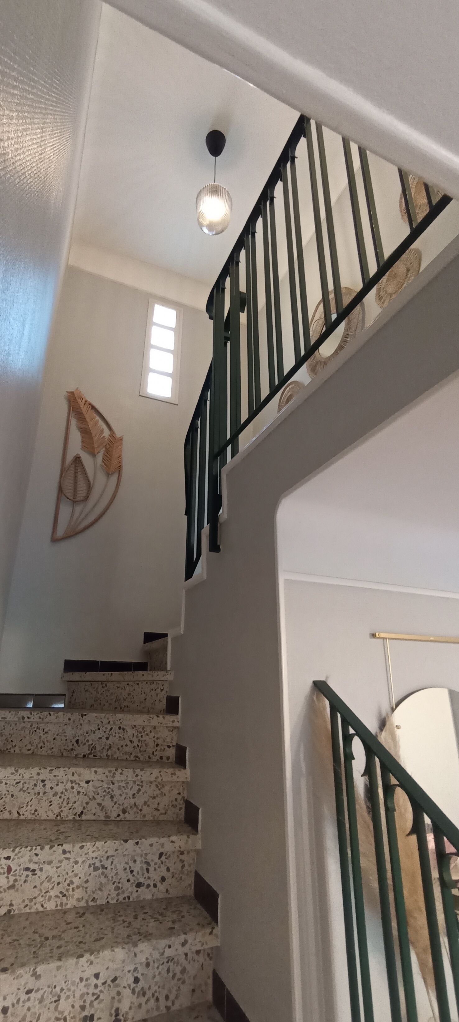 A staircase with a speckled floor, a green metal railing, and a wall-mounted light fixture.
