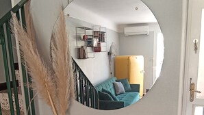 Een spiegel op een dressoir, met een vaas met pluizige grasjes, een glazen vaas en een gevlochten mand.