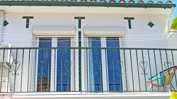 Een gebouw met twee verdiepingen, een balkon, een eethoek met tafel en stoelen, en een schuifdeur naar de binnenruimte.
