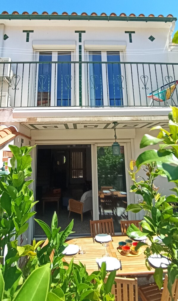 Ein zweistöckiges Gebäude mit einem Balkon, einem Essbereich inklusive Tisch und Stühlen sowie einer Glasschiebetür, die zu einem Innenraum führt.