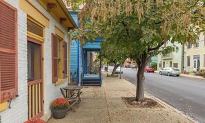 Une vue de rue avec un immeuble doté d’un porche, d’un arbre et de voitures garées.
