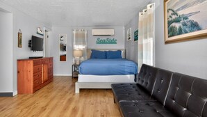 A bedroom with a bed, a wooden dresser, a black leather sofa, a TV, and a painting on the wall.
