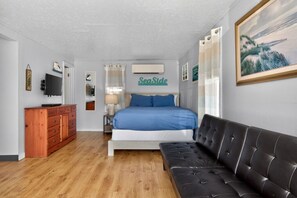 Ein Schlafzimmer mit einem Bett, einer Holzkombination, einem schwarzen Ledersofa, einem Fernseher und einem Bild an der Wand.