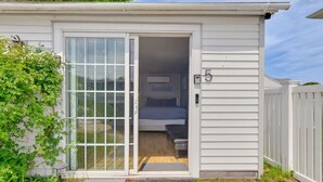 A small, single-room mobile home with a sliding glass door entrance, a bed, and a small bench.