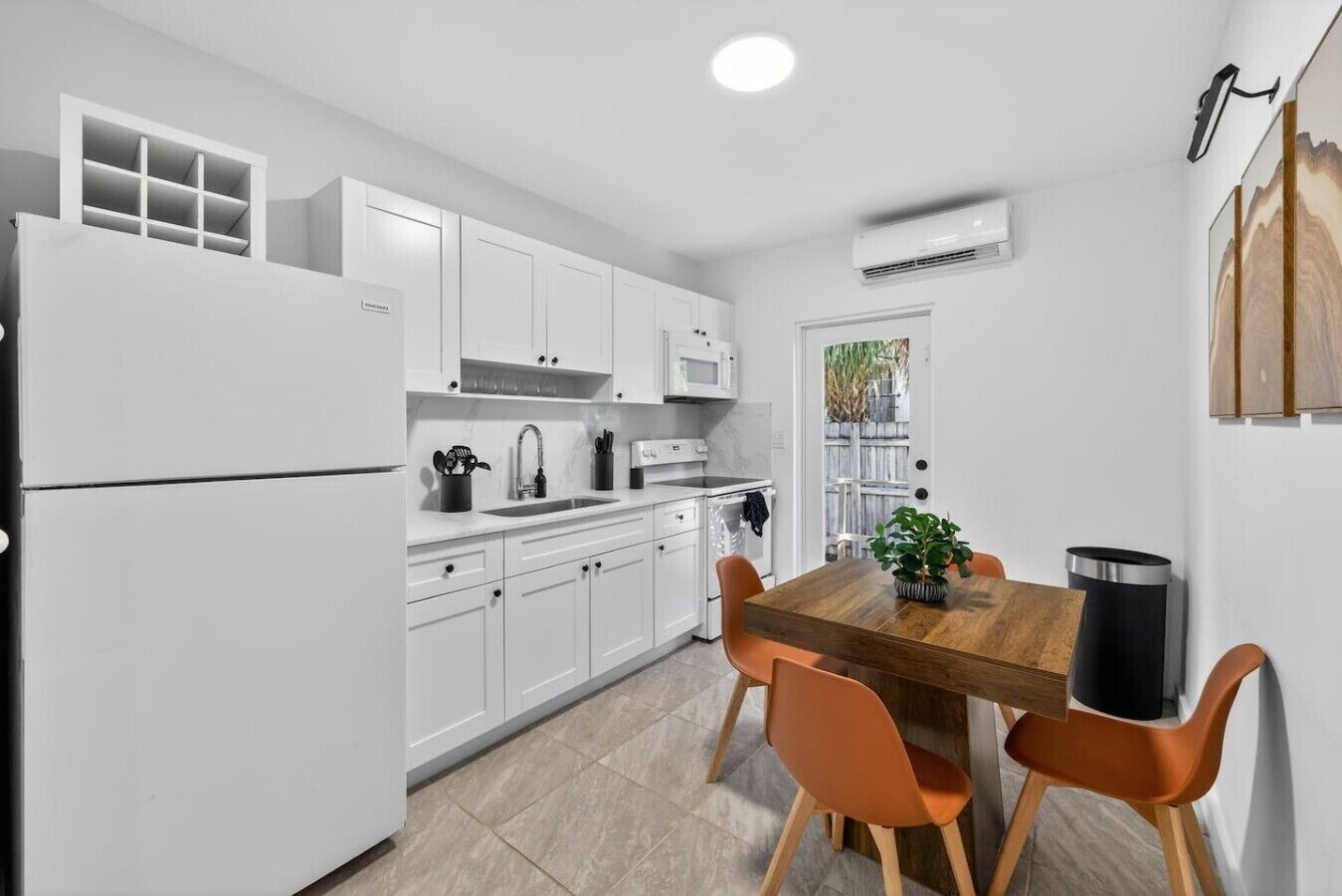 A modern kitchen with white cabinets, a wooden dining table, and orange chairs.