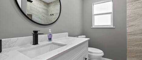 A bathroom with a white vanity, a round mirror, a toilet, and a window.