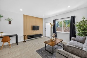 Ein Wohnzimmer mit Fernseher, Sofa, Couchtisch, Schreibtisch und einer Pflanze.