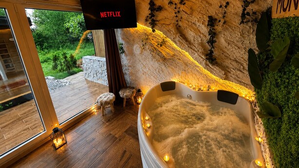 A modern bathroom with a stone wall, a bathtub, and a Netflix sign. - Cozy Chalet with Jacuzzi, Heated pool & Sauna Montebliss (Miljevići)