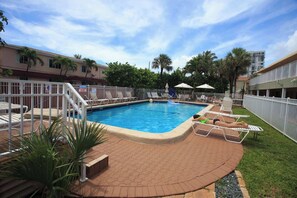 A swimming pool with lounge chairs, a fenced area, and a building in the background. - Oceanview Retreat in Hollywood Beach (Hollywood)