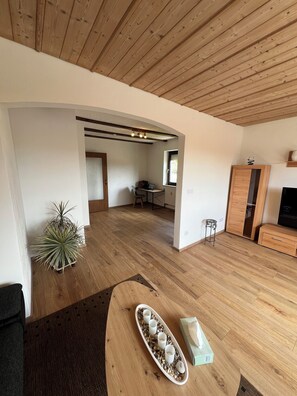 Ein geräumiger Wohnbereich mit Holzboden, einem Esstisch mit Tassen, einem Blumentopf und einem TV-Schrank.