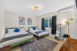 Ein Zimmer mit zwei Betten, einer Stehlampe, einem Spiegel und einem Fenster mit Vorhängen.