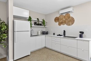 Eine moderne Küche mit weißen Schränken, einem eingebauten Kühlschrank, einer Mikrowelle, einem Spülbecken und einer Wand-Klimaanlage.