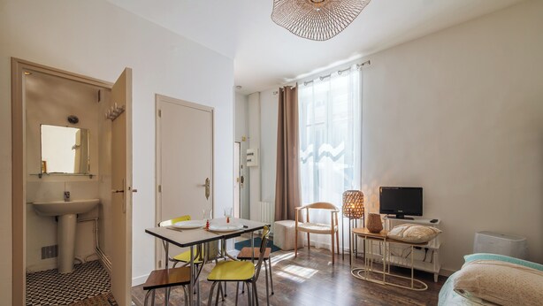 A room with a dining table, chairs, a bed, a TV, and a bathroom with a sink and mirror. - Le Rousseau - Petfriendly - Wifi - TV (Laval)