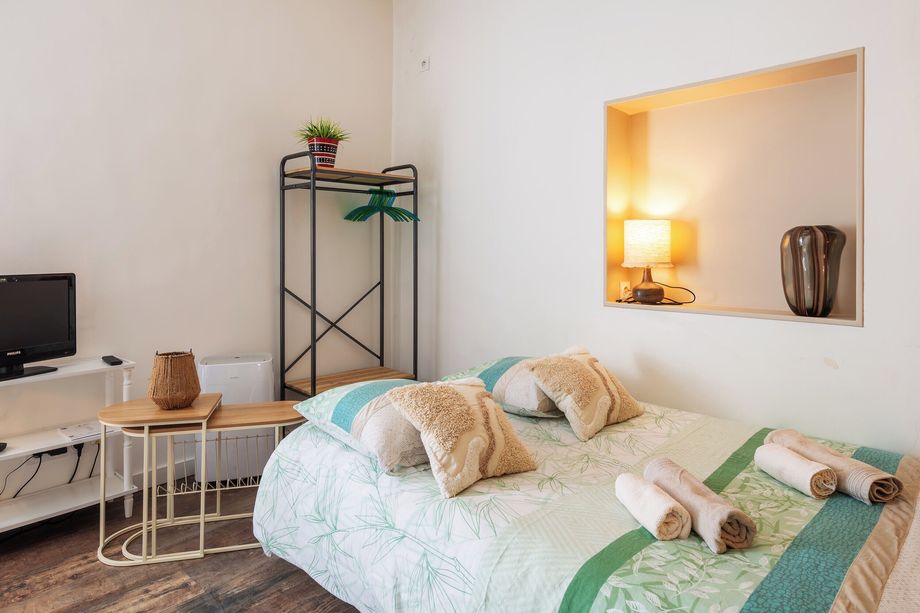 Ein Hotelzimmer mit Bett, Schreibtisch, Fernseher, Spiegel und einer Wandlampe.