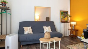 A living room with a grey sofa, a small white table, a standing heater, a radiator, and a painting on the wall. - Le Rousseau - Petfriendly - Wifi - TV (Laval)