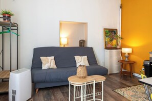 Ein Wohnzimmer mit grauem Sofa, einem kleinen weißen Tisch, einem Standheizgerät, einer Heizung und einem Bild an der Wand.