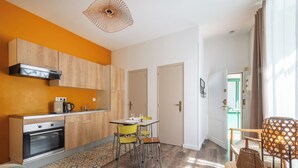 A compact kitchen with wooden cabinets, a built-in oven, and a dining area with chairs and a table. - Le Rousseau - Petfriendly - Wifi - TV (Laval)