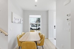 A modern room with a wooden table and yellow chairs, a window with a view of a parked car, and a white door. - Beautiful 3BR Getaway in Trendy NW Calgary (Calgary)