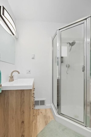 Ein modernes Badezimmer mit Duschkabine aus Glas, einem weißen Waschbecken mit Holzschublade und einem Spiegel darüber.