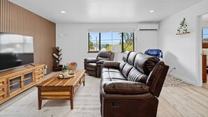 Un salon moderne doté d’un téléviseur à écran plat, d’un canapé en cuir, d’une table basse en bois et offrant une vue sur l’extérieur grâce à de grandes fenêtres.