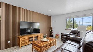 Un salon moderne avec un téléviseur, un meuble de rangement en bois, un canapé en cuir et une grande fenêtre.
