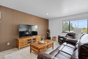 Ein modernes Wohnzimmer mit Fernseher, Holzschrank, Ledersofa und großem Fenster.