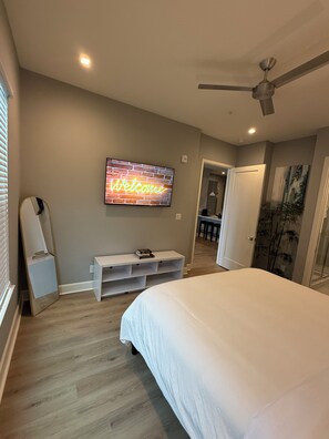 A bedroom with a bed, a TV mounted on the wall, a ceiling fan, and a door leading to another room. - Luxury Modern King Bed Heart of Downtown Dallas (Dallas)