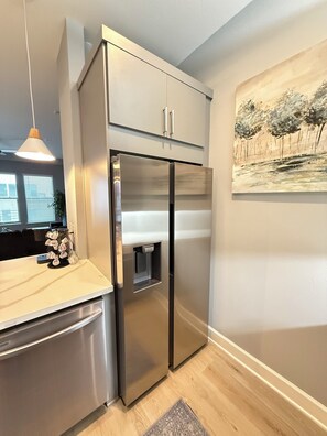 A modern kitchen with a stainless steel refrigerator, a built-in water dispenser, and a pendant light.