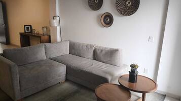 Una sala de estar con un sofá seccional gris, una mesa de centro redonda de madera y dos placas decorativas colgadas en la pared.