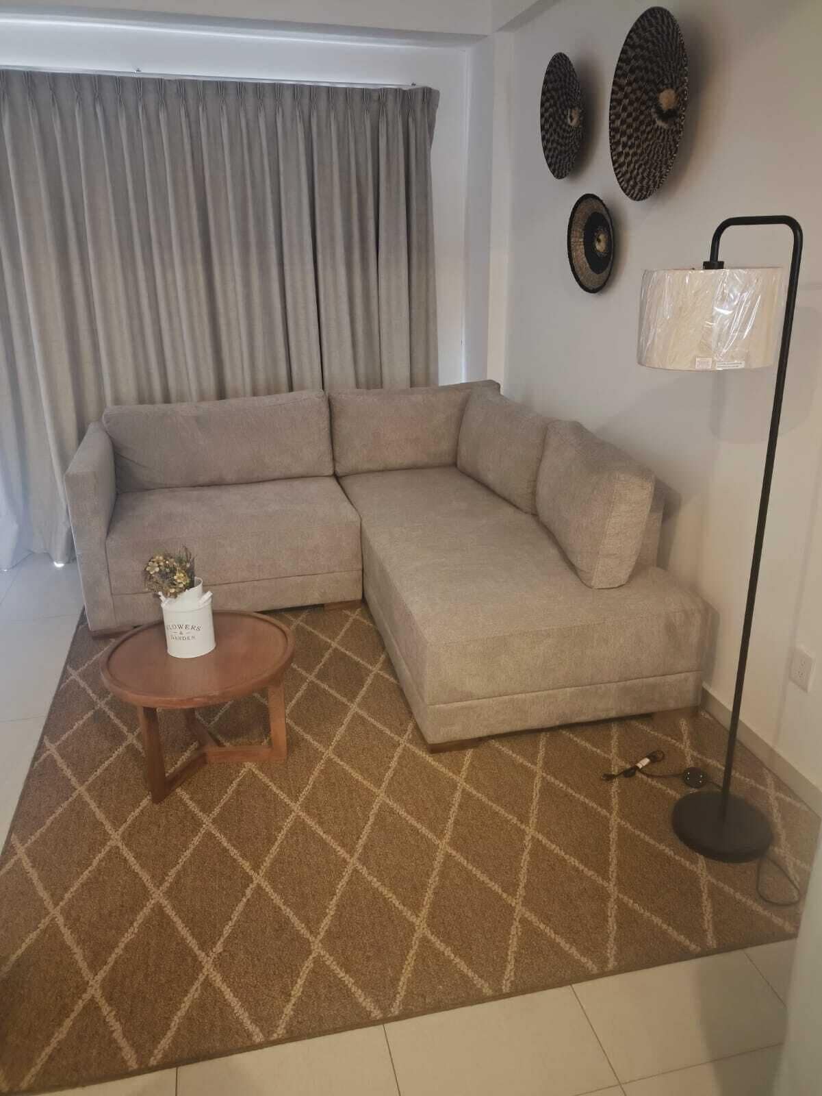 Una sala de estar con un sofá modular, una mesita de centro de madera, una lámpara de pie y una alfombra estampada.