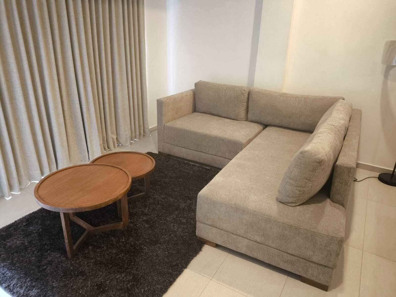 Ein Wohnzimmer mit einer Eckcouch, einem runden Holztisch und einem dunklen Teppich.