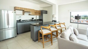 A modern kitchen with a central island, wooden chairs, a sofa, and a view through a window. - Suites Santa Isabella (Ajijic)